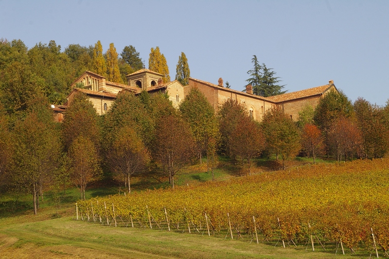 Veduta dal basso della facciata principale della Canonica di Santa Maria di Vezzolano, immersa nella vegetazione arborea ed arbustiva nella vivace colorazione autunnale.
