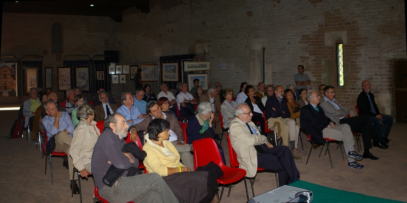 Veduta del folto ed attento pubblico presente in sala e sullo sfondo la Mostra di dipinti su "Abbazie e luoghi del Piemonte" dell artista Gabriella Arduino.